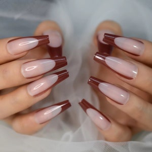 Puede incluir: Uñas postizas en forma de ataúd con diseño de manicura francesa. Las uñas tienen una base transparente y una punta marrón oscuro. Las uñas son largas y rectangulares, con un acabado brillante.