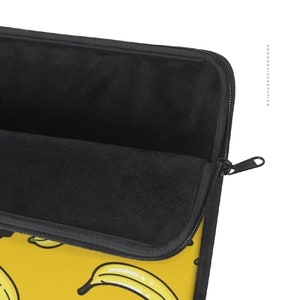 May include: A black laptop sleeve with a zipper closure. The sleeve has a yellow background with a repeating pattern of yellow bananas. The inside of the sleeve is lined with black fleece.