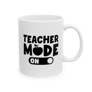 May include: White ceramic mug with the words "TEACHER MODE ON" in black, with an apple graphic in the center. The mug has a standard handle and is suitable for hot or cold beverages.