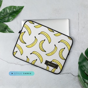 May include: White laptop sleeve with a black zipper and a repeating pattern of yellow bananas. The sleeve has the text "BRITNEY" on the bottom right corner.
