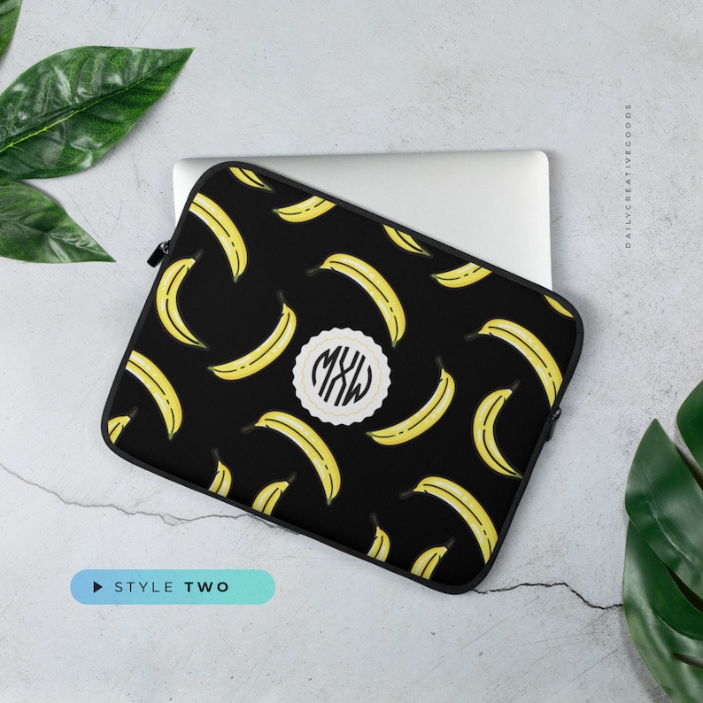 May include: Black laptop sleeve with a yellow banana pattern and a white circle with the monogram "MXW" in black. The sleeve is on a gray surface.