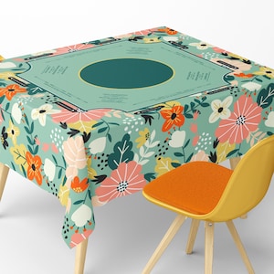 May include: A floral tablecloth with a teal background and a repeating pattern of flowers in orange, pink, yellow, and white. The tablecloth has a central teal section with text and a gold border. A yellow chair with an orange seat is in the foreground.