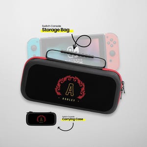 May include: Black and red carrying case for a Nintendo Switch console with a personalized monogram of the letter "A" in a gold wreath with the name "Ashley" underneath. The case has a zipper and a handle. The image also shows a smaller black carrying case with the same monogram.