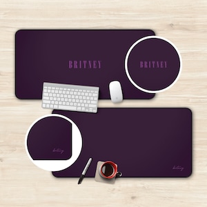 May include: Two purple desk mats with the name "BRITNEY" printed in a light purple colour. The top mat has a circle with the same text in the centre. The bottom mat has the name written in cursive in the bottom right corner.