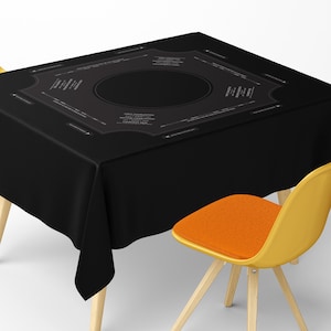 Könnte beinhalten: Ein schwarzes Tischtuch mit detailliertem Design, das Text und ein zentrales Oval aufweist. Das Tischtuch ist über einen Tisch mit Holzbeinen drapiert. Ein gelber Stuhl mit orangefarbener Sitzfläche befindet sich im Vordergrund.