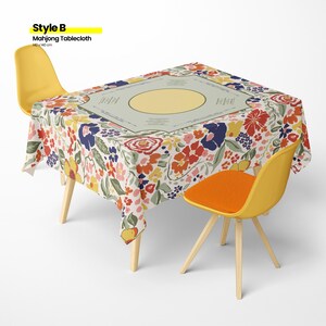 May include: A floral Mahjong tablecloth, 55 x 55 inches, covers a table. The tablecloth features a cream background with red, blue, and yellow flowers. Two yellow chairs with wooden legs and an orange seat cushion are positioned around the table. The text "Style B Mahjong Tablecloth" is in the upper left corner.