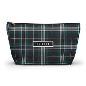 May include: A rectangular cosmetic bag with a black, teal, and white plaid pattern. The bag has a gold zipper and the name "BRITNEY" in a white rectangle on the front.