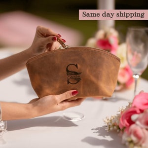 May include: A brown leather makeup bag with a zipper closure. The bag is personalized with the letter "S" and the name "Shirley" in a floral design.