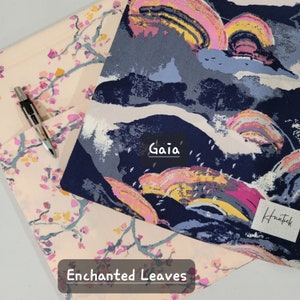 Op de afbeelding: Een roze en blauwe stof met een kleurrijk abstract ontwerp. De stof heeft de woorden "Gaia" en "Huntek" erop gedrukt. De stof is gelabeld met "Enchanted Leaves".