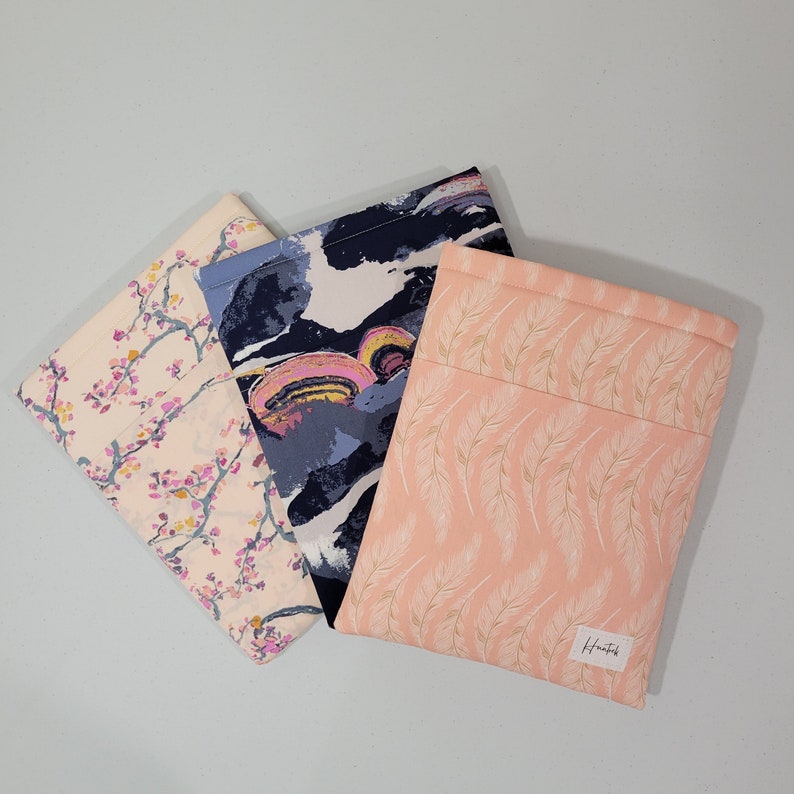 Op de afbeelding: Drie stoffen zakjes met verschillende patronen. Het eerste zakje is roze met een wit bloemenpatroon. Het tweede zakje is blauw, wit en roze met een draaiend abstract patroon. Het derde zakje is perzikkleurig met een wit verenpatroon en de tekst "Hunt & Gather" gedrukt in de rechterbenedenhoek.