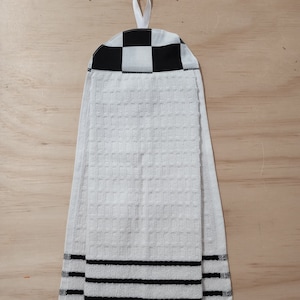 May include: White kitchen towel with black stripes and a checkered black and white fabric loop at the top.