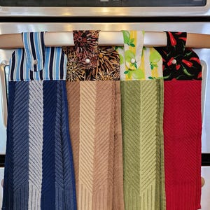 May include: Four kitchen towels hanging on a rack. The towels are made of a soft, absorbent material and feature different patterns. The first towel is blue and white striped, the second is brown with a floral pattern, the third is green with a lemon pattern, and the fourth is red with a chili pepper pattern.