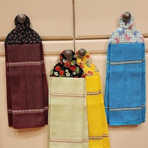 May include: Four kitchen towels hanging on hooks. The towels are in different colors and patterns, including red, green, yellow, and blue. The towels are all made of a soft, absorbent material.