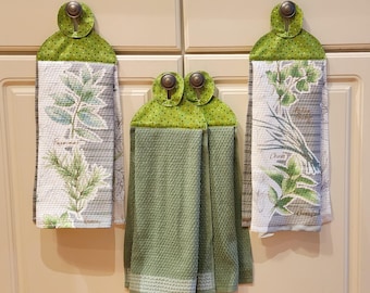 May include: Set of four green kitchen towels with a green and white polka dot trim. The towels have a floral design with the names of herbs printed on them. The towels are hanging on hooks.