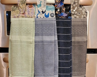 May include: Four kitchen towels hanging on a silver oven handle. The towels are made of a soft, absorbent fabric and have different patterns. The towels are green, blue, black, and brown.
