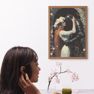 May include: A framed painting of a woman in a white dress with a crown of white flowers on her head, embracing a knight in black armor. The painting is set against a backdrop of a garden with green foliage and pink flowers.