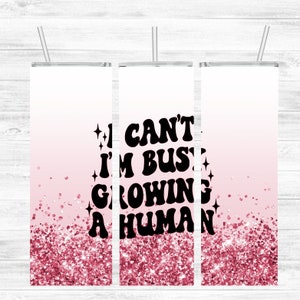 May include: Three stainless steel tumblers with a pink glitter ombre design. The middle tumbler has the text "I CAN'T I'M BUSY GROWING A HUMAN" in black.