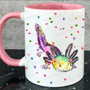 Pu&ograve; includere: Una tazza in ceramica bianca con un manico rosa presenta un'illustrazione colorata di un axolotl con un motivo arcobaleno. Lo sfondo &egrave; bianco con cuori rosa, blu, verdi e viola sparsi.