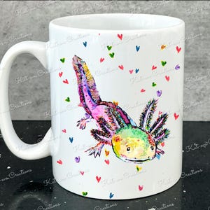 Pu&ograve; includere: Tazza in ceramica bianca con un'illustrazione colorata di un axolotl con colori arcobaleno e accenti rosa. L'axolotl &egrave; circondato da piccoli cuori di vari colori.