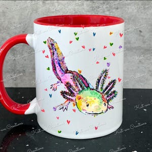 Pu&ograve; includere: Una tazza in ceramica bianca con bordo e manico rossi. La tazza presenta un'illustrazione colorata di un axolotl con colori rosa, verde e giallo. Lo sfondo &egrave; bianco con cuori rosa, verdi e blu sparsi.