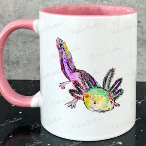 Pu&ograve; includere: Una tazza in ceramica bianca con un manico e un bordo rosa. La tazza presenta un'illustrazione colorata di un axolotl, un tipo di salamandra, con colori rosa, verde, giallo e blu.