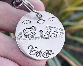 May include: Silver key chain with a round tag featuring two sheep and the word "Beleza" engraved on the bottom.