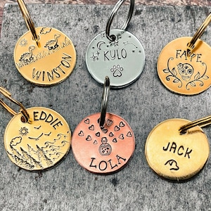 Op de afbeelding: Zes verschillende hondenpenningen van goud, zilver en koper met gegraveerde namen en ontwerpen. De penningen hebben namen zoals "Winston", "Eddie", "Lola", "Jack", "Faye" en "Kylo".