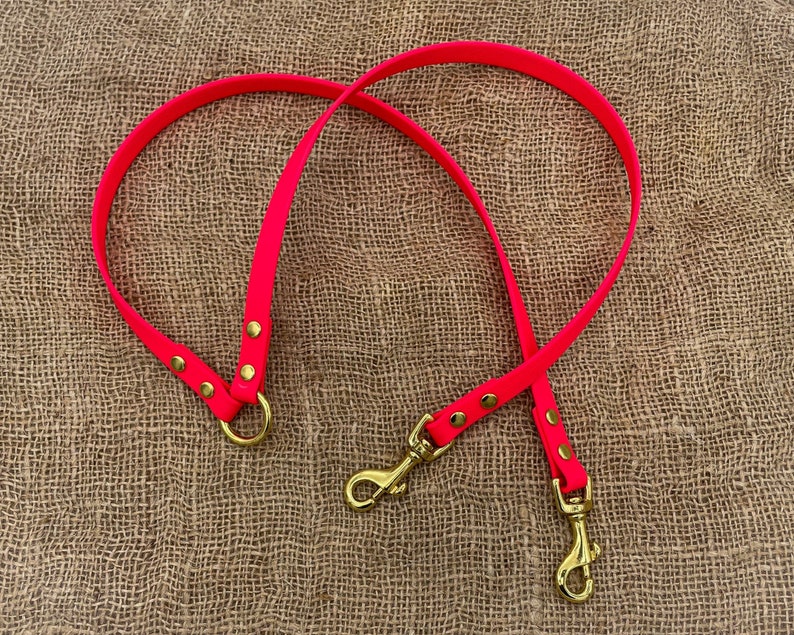 May include: A bright pink dog lead with two gold metal clips. The lead is made of a durable material and is perfect for walking your dog.