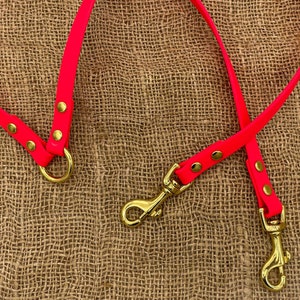 May include: Two bright pink dog leads with gold metal clips and rings. The leads are on a brown hessian background.