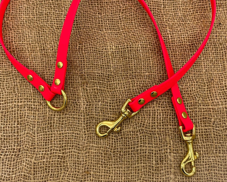May include: Two bright pink dog leads with gold metal clips and rings. The leads are on a brown hessian background.
