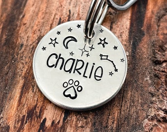 May include: Silver dog tag with a paw print, a crescent moon, stars, and the name "charlie" engraved on it.