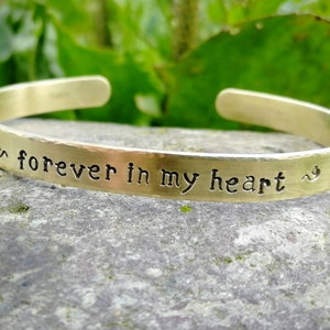 May include: A gold-toned metal bracelet with the inscription "& forever in my heart ~".
