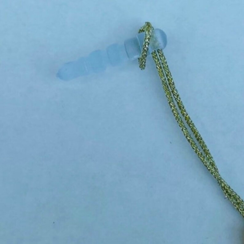 Op de afbeelding: Een doorzichtige oordop van plastic met een gouden koord eraan. De oordop is ontworpen om geluid te blokkeren.