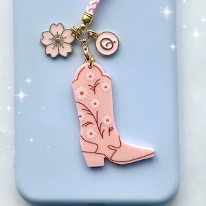 May include: Pink cowboy boot charm with a floral design, attached to a pink and gold chain with a pink flower and a pink letter Q charm.