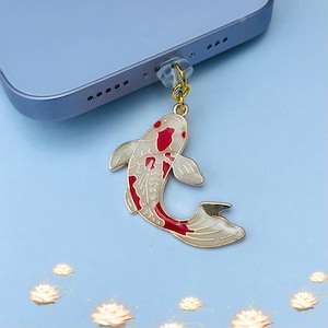 May include: A gold-coloured phone charm featuring a red and white koi fish design. The charm is attached to a clear plastic phone jack adapter.