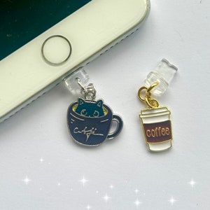 May include: Two phone charms, one with a black cat peeking out of a blue and silver coffee cup with the word "coffee" written on it, and the other with a brown and white coffee cup with the word "coffee" written on it.