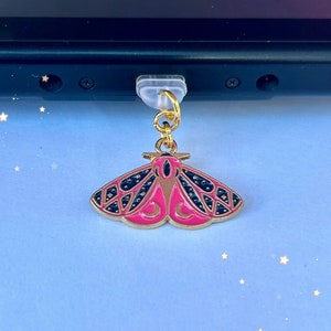May include: A pink and black moth charm with gold accents. The charm is attached to a gold chain and a clear plastic connector. The charm is hanging from a black Nintendo Switch.