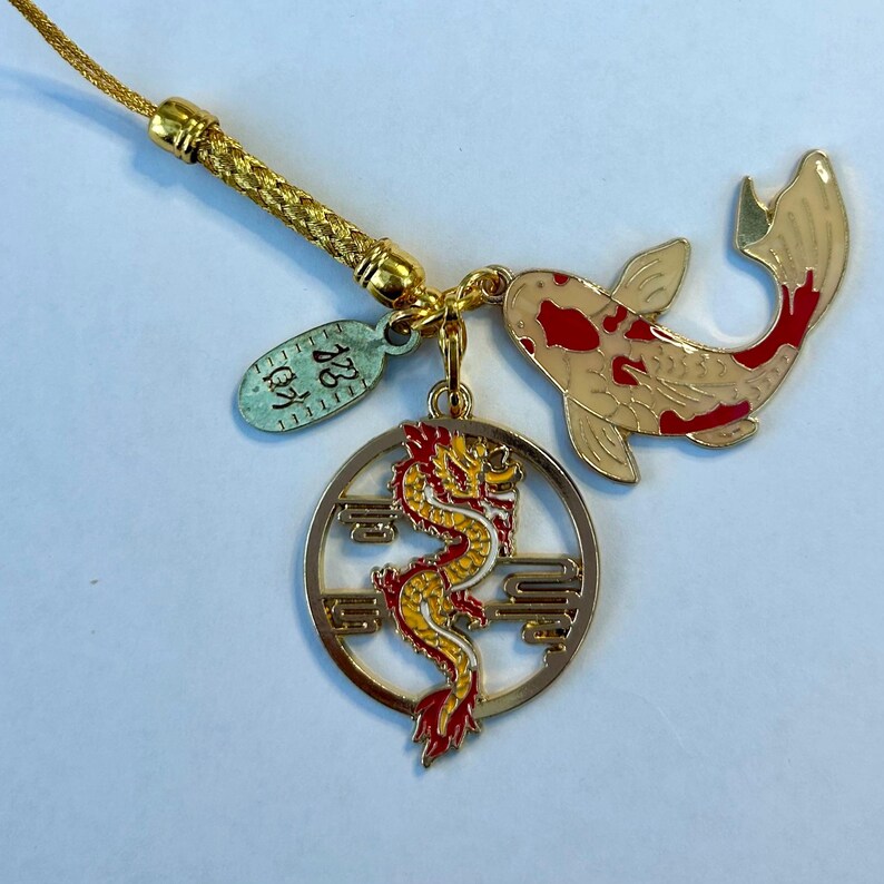 Op de afbeelding: Gouden bedel met een rode en gele draak, een witte en rode koi-vis en een tag met de tekst "128 12".
