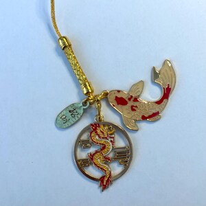 Op de afbeelding: Gouden bedel met een rood-witte koi-vis, een gele draak in een cirkel en een klein ovaal label met de tekst "22K".