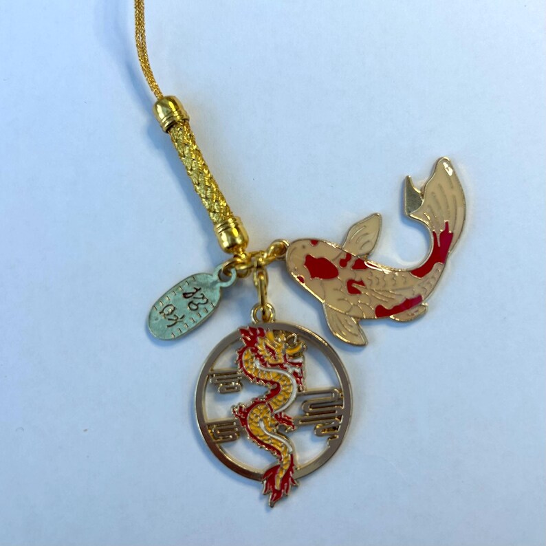 Op de afbeelding: Gouden bedel met een rood-witte koi-vis, een gele draak in een cirkel en een klein ovaal label met de tekst "22K".