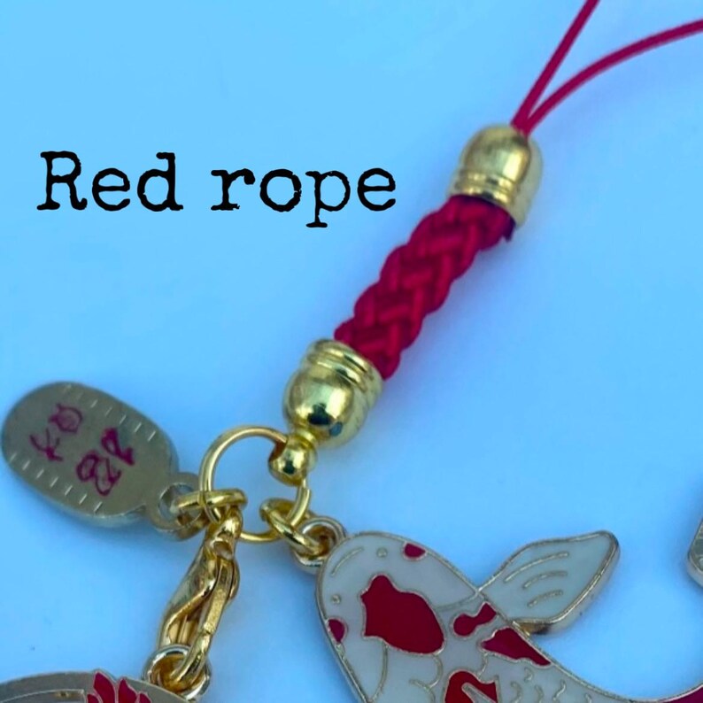 Op de afbeelding: Een rode gevlochten touwtjes sleutelhanger met gouden kralen en een bedel met een rode en witte koi-vis. De bedel heeft ook een klein gouden label met Chinese karakters.