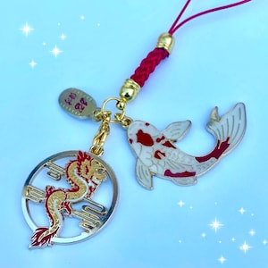 Op de afbeelding: Een gouden bedel met een rood en gouden drakenontwerp, een witte en rode koi-visbedel en een gouden bedel met de tekst "Kyo 22" in rood. De bedels zijn bevestigd aan een rood gevlochten koord.