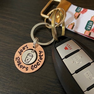 May include: A copper keychain with the words "Coffee Society" and "Keep Calm and Drink Coffee" engraved on it. The keychain is attached to a silver key ring and a car key.