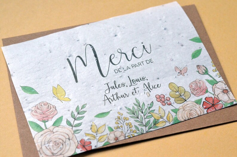 May include: A white card with a brown border and a floral design. The card has the text 'Merci de la part de Jules, Louis, Arthur et Alice'.