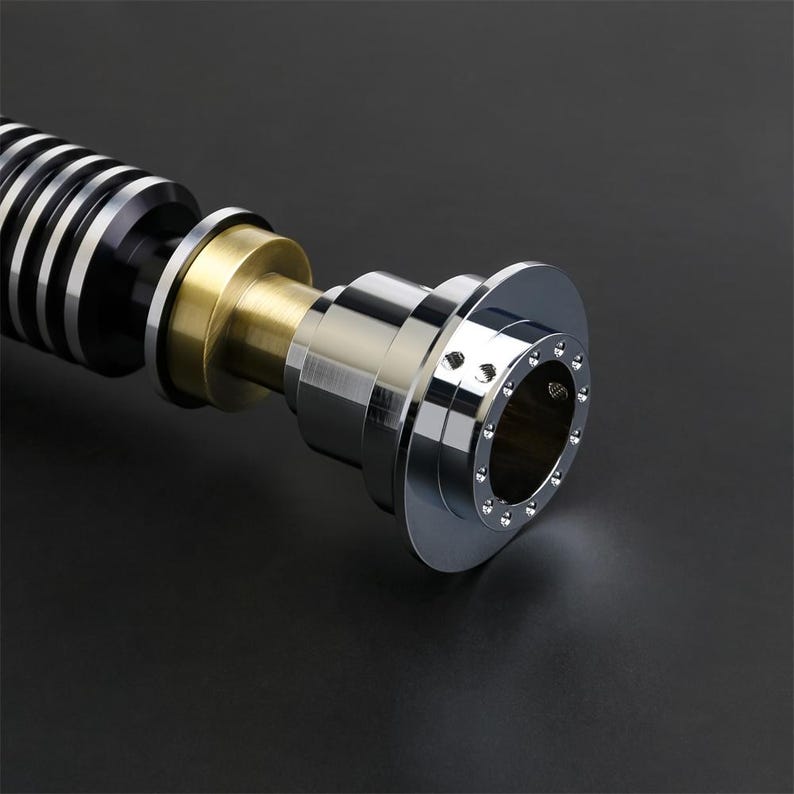 May include: A close-up of a lightsaber hilt with a black and silver body, a gold accent, and a chrome end cap with a ring of small holes.