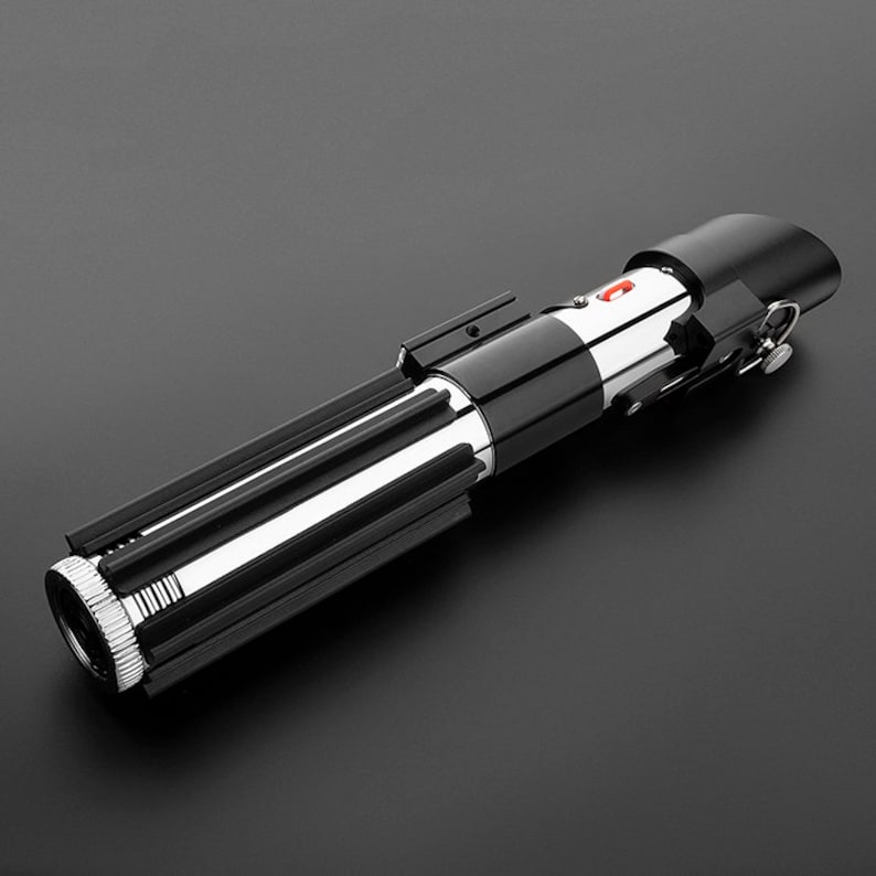 Op de afbeelding: Een zwart en zilveren lightsaber-speelgoed met een rode knop op de handgreep.