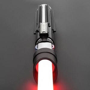 Op de afbeelding: Een zwart lightsaber met een rode blade. De lightsaber heeft een zilveren metalen handvat en een zwarte grip.