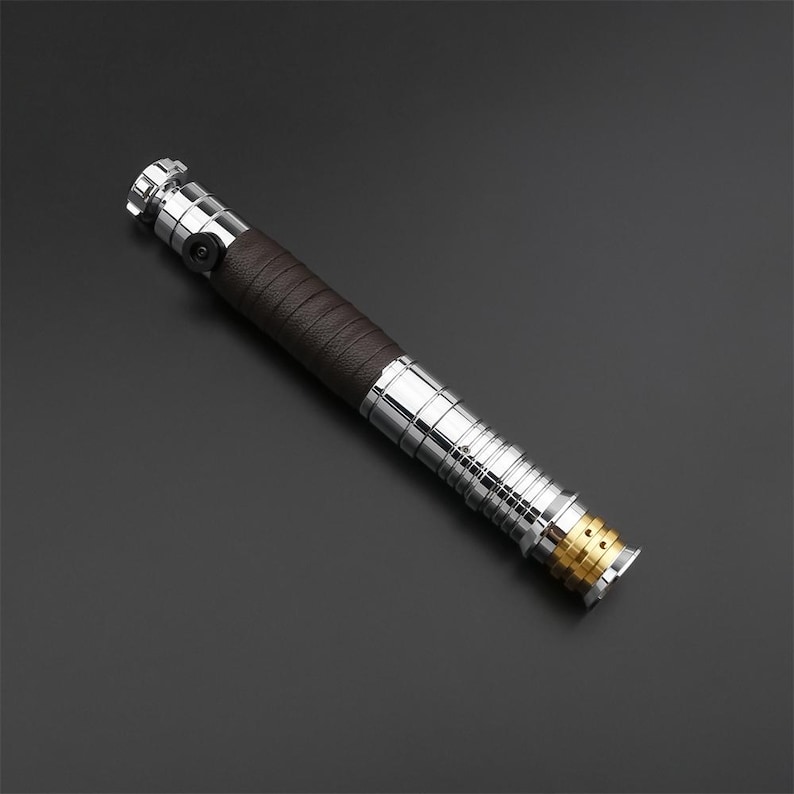 May include: A silver and brown lightsaber with a gold accent at the end. The lightsaber has a textured brown grip.