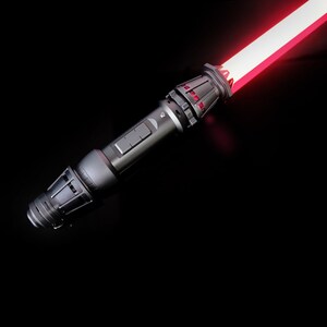 May include: A black lightsaber with a red blade. The lightsaber has a textured handle with a silver accent.