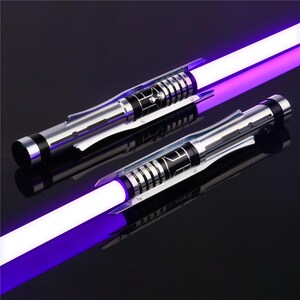May include: Two silver and black lightsaber hilts with purple blades. The hilts have a textured, metallic finish and a series of black rings.
